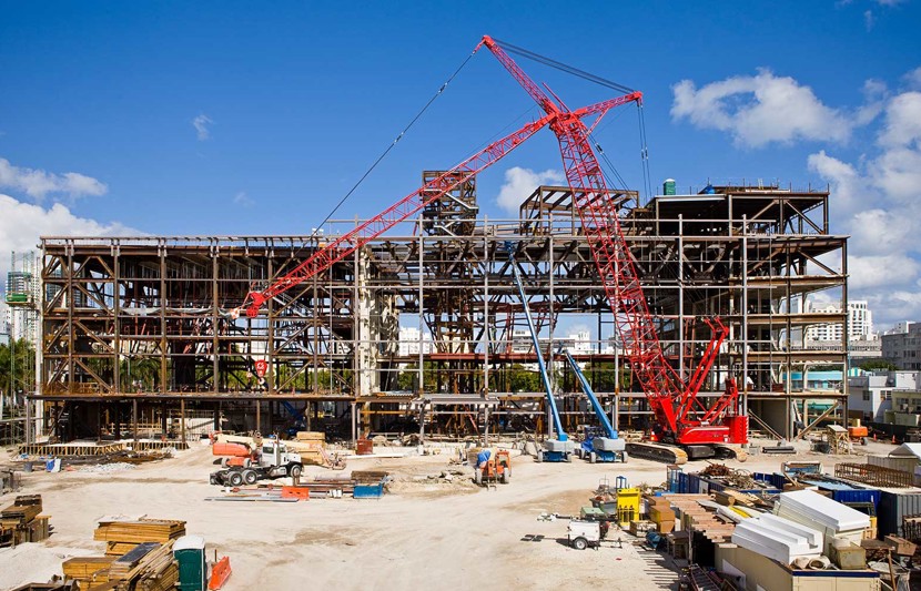 Working construction site on a sunny day with a red crane, various vehicles, and building materials stacked ready for use in the foreground.