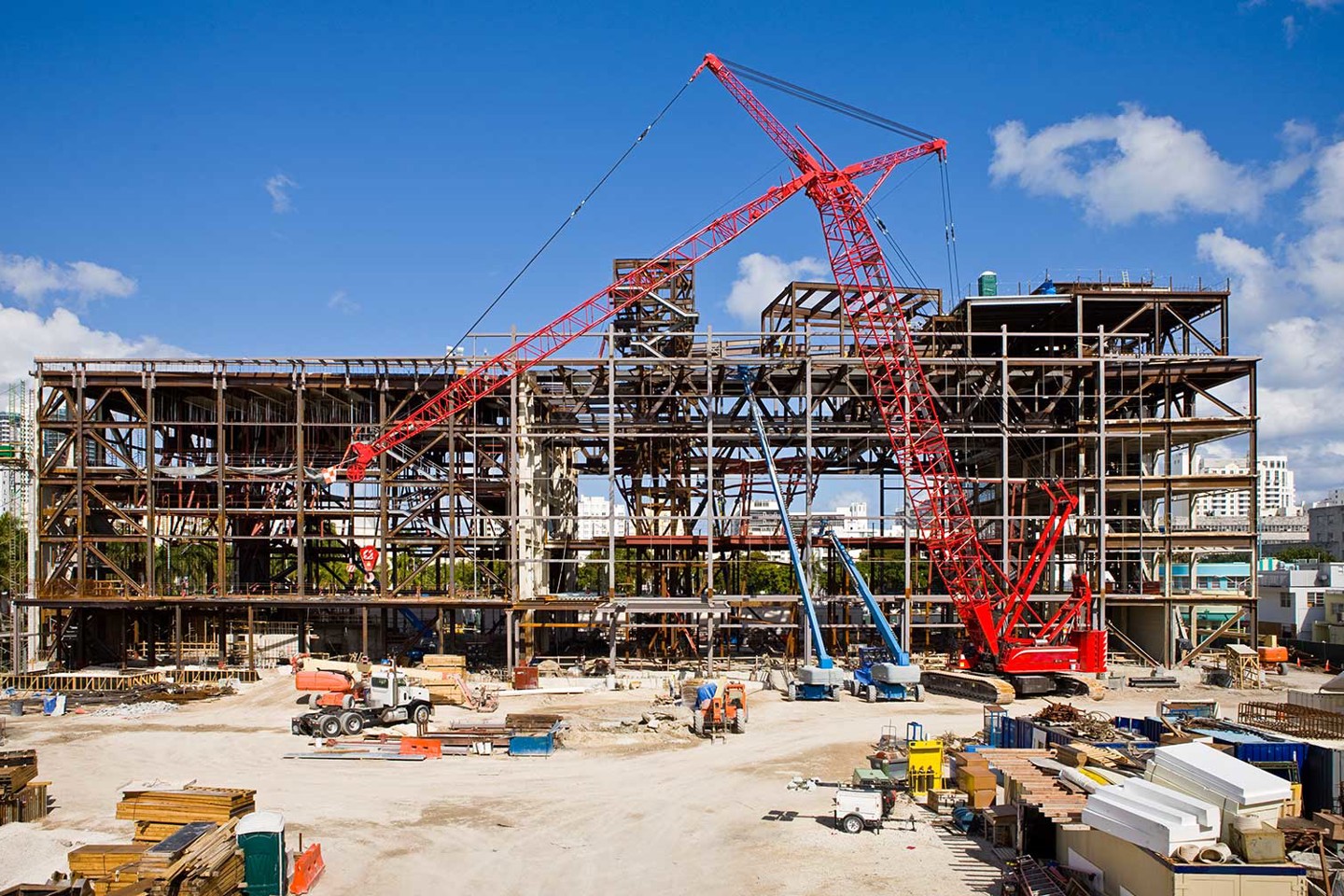 Working construction site on a sunny day with a red crane, various vehicles, and building materials stacked ready for use in the foreground.