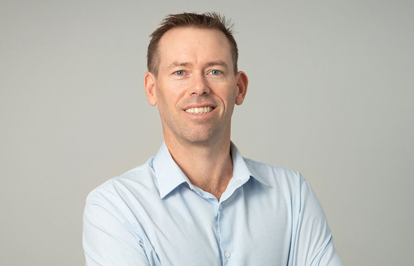 RPS Senior Principal Surveyor and Registered Surveyor, David Ada, smiles at the camera with crossed arms. Light blue shirt and grey background.