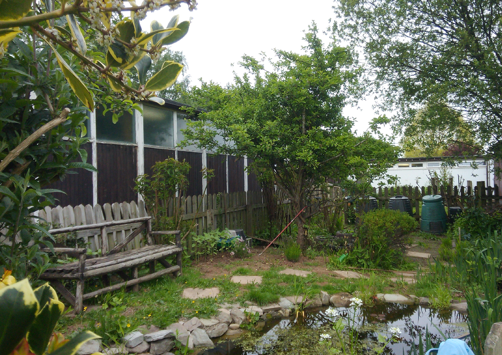 School garden with wooden bench and pond with a water butt.