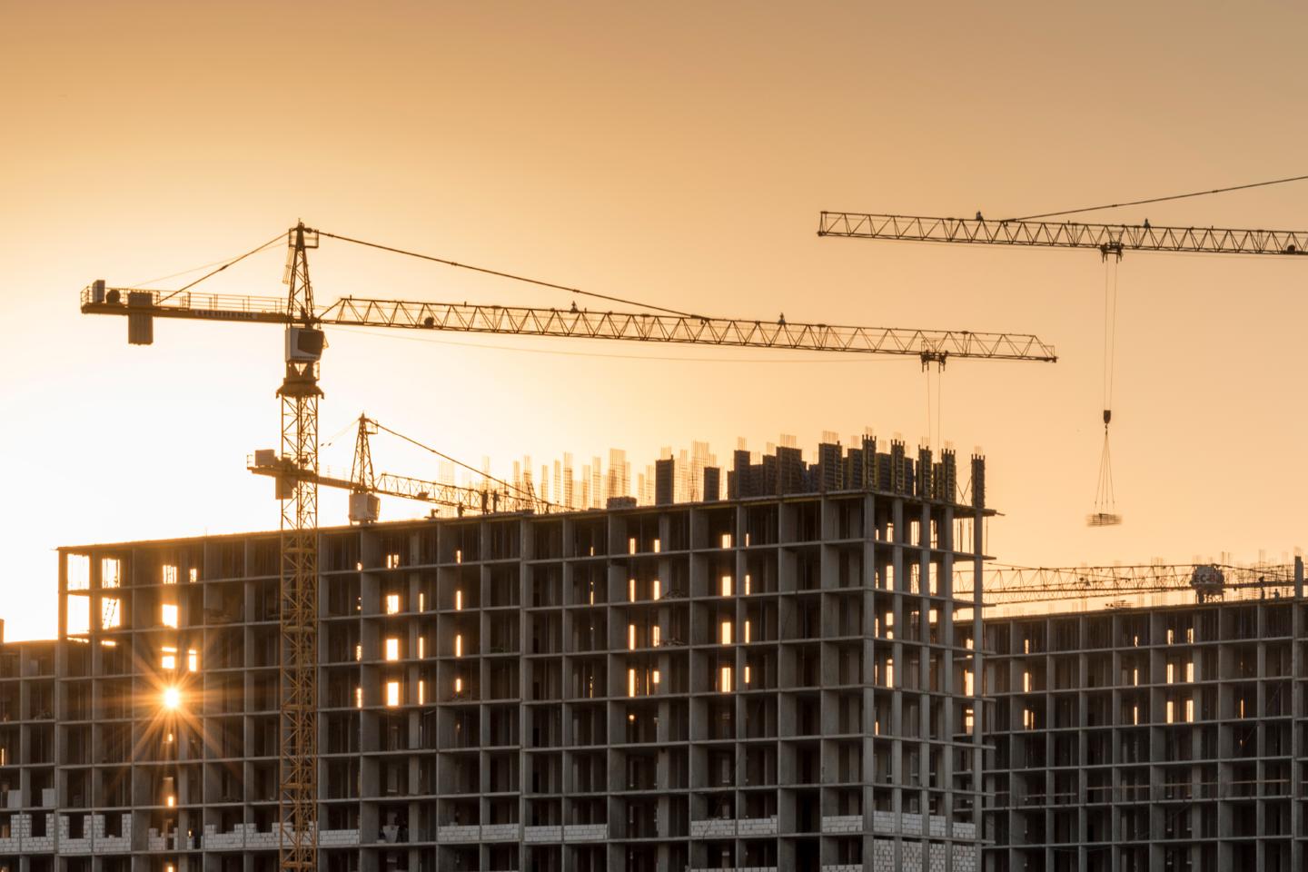 Building under construction at dusk. Orange sunset and cranes in the shadows