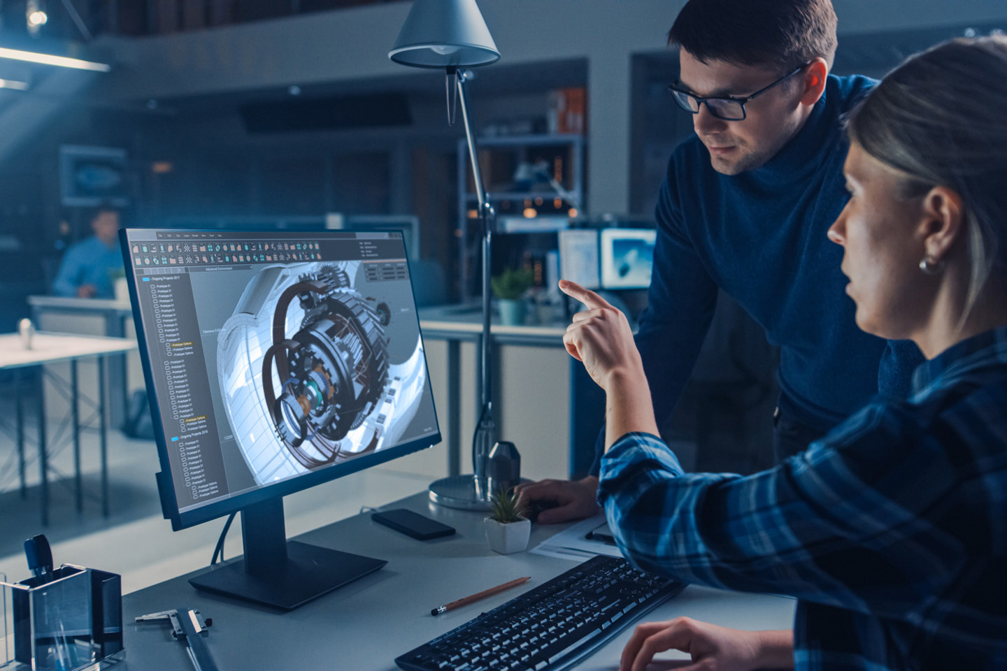 Systems engineer talking to designer over computer with CAD rendered turbine components on screen