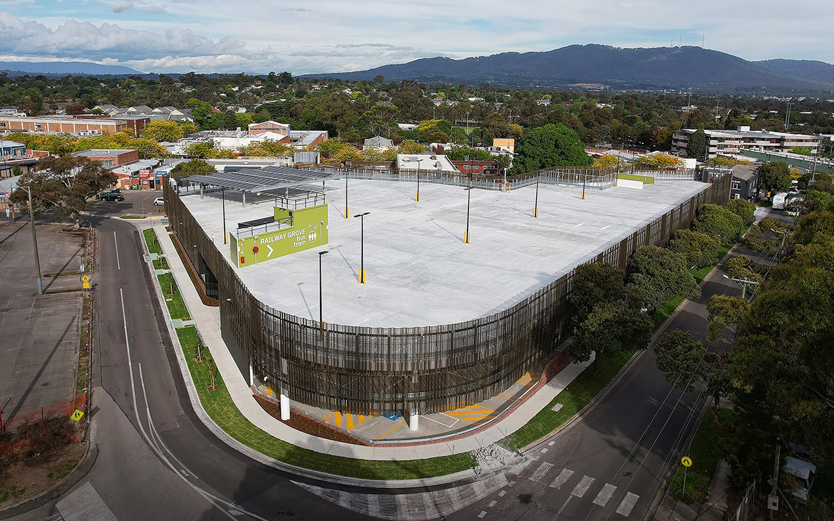 Aerial photograph taken on a sunny day looking downward over the rooftop of the Devon Street car parking facility. Solar panel array in the lefthand corner of the roof, and suburb of Croydon and mountains beyond in the background.
