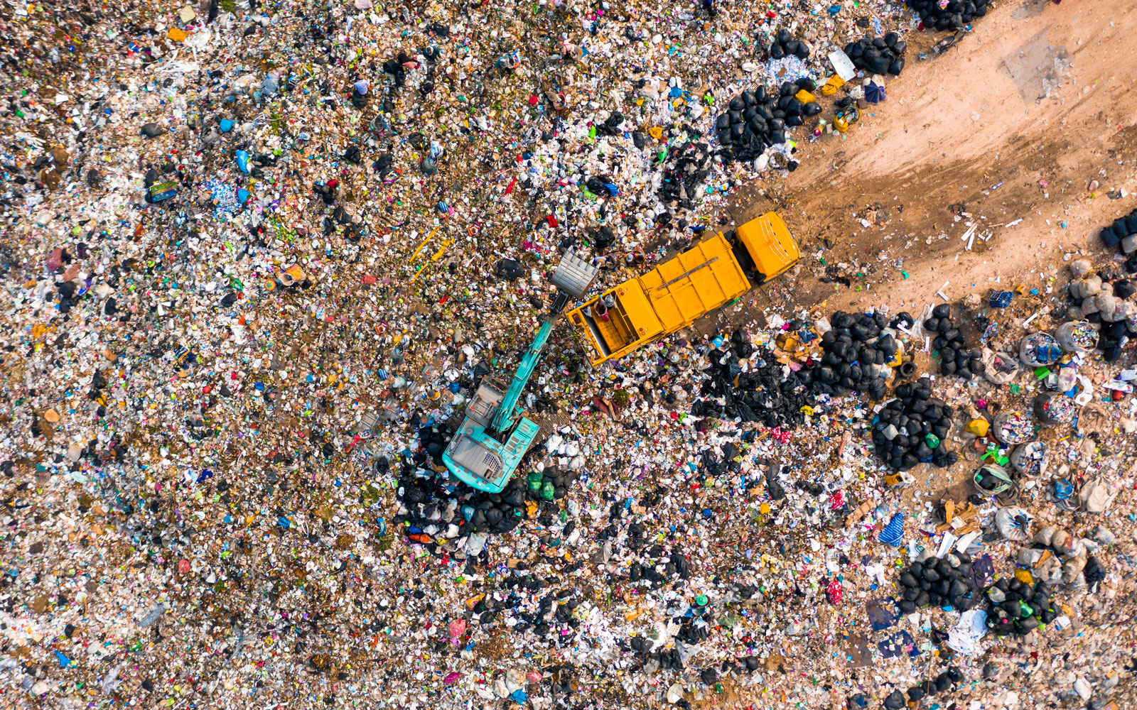 A birds eye view of two dump trucks working in a landfill site surrounded by thousands of plastic items 