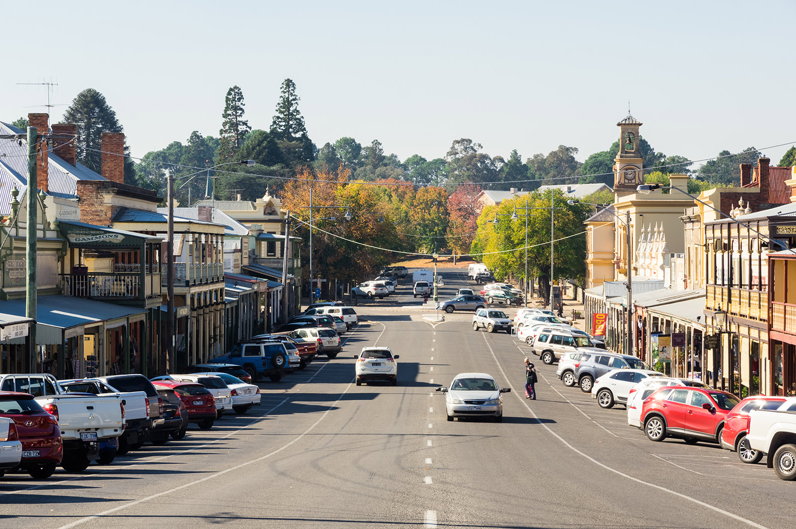 Cars drive down the main street and people wait to cross the road in a small regional Australian town. 