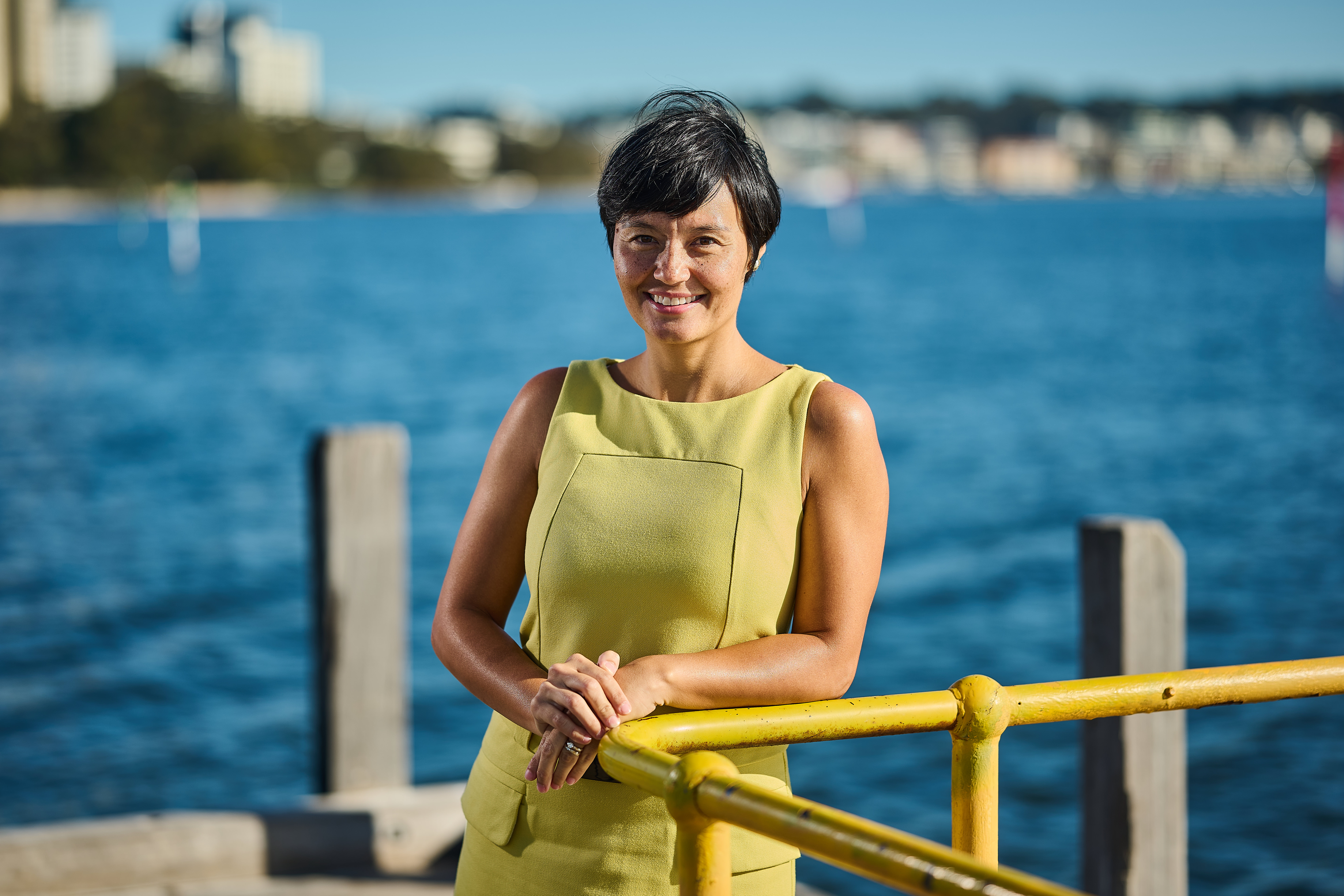 RPS Operations Environmental Manager, Jemaville Lim wears a yellow dress and stands on a jetty with Perth city in the background.  