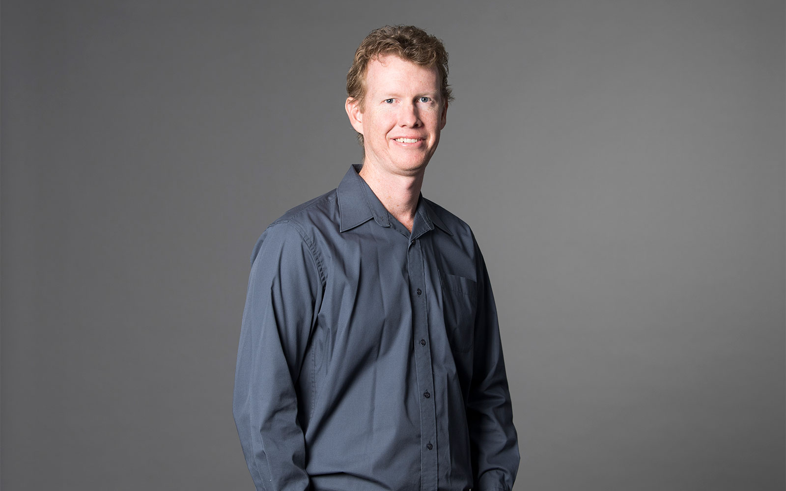 Simon Sager, RPS Principal Surveyor smiles at the camera wearing a grey button up shirt