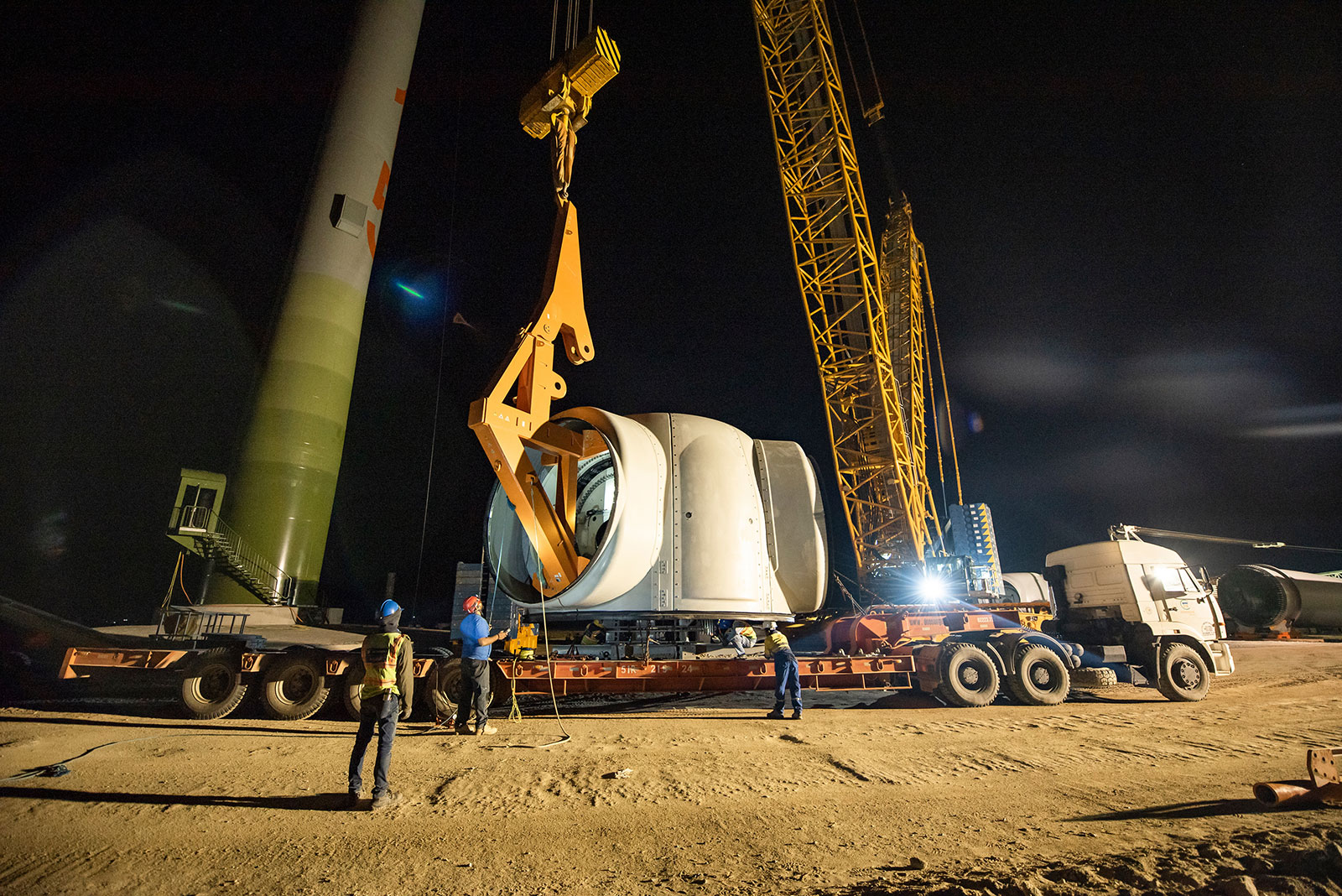 Construction team works to install a wind turbine at night using a large crane.