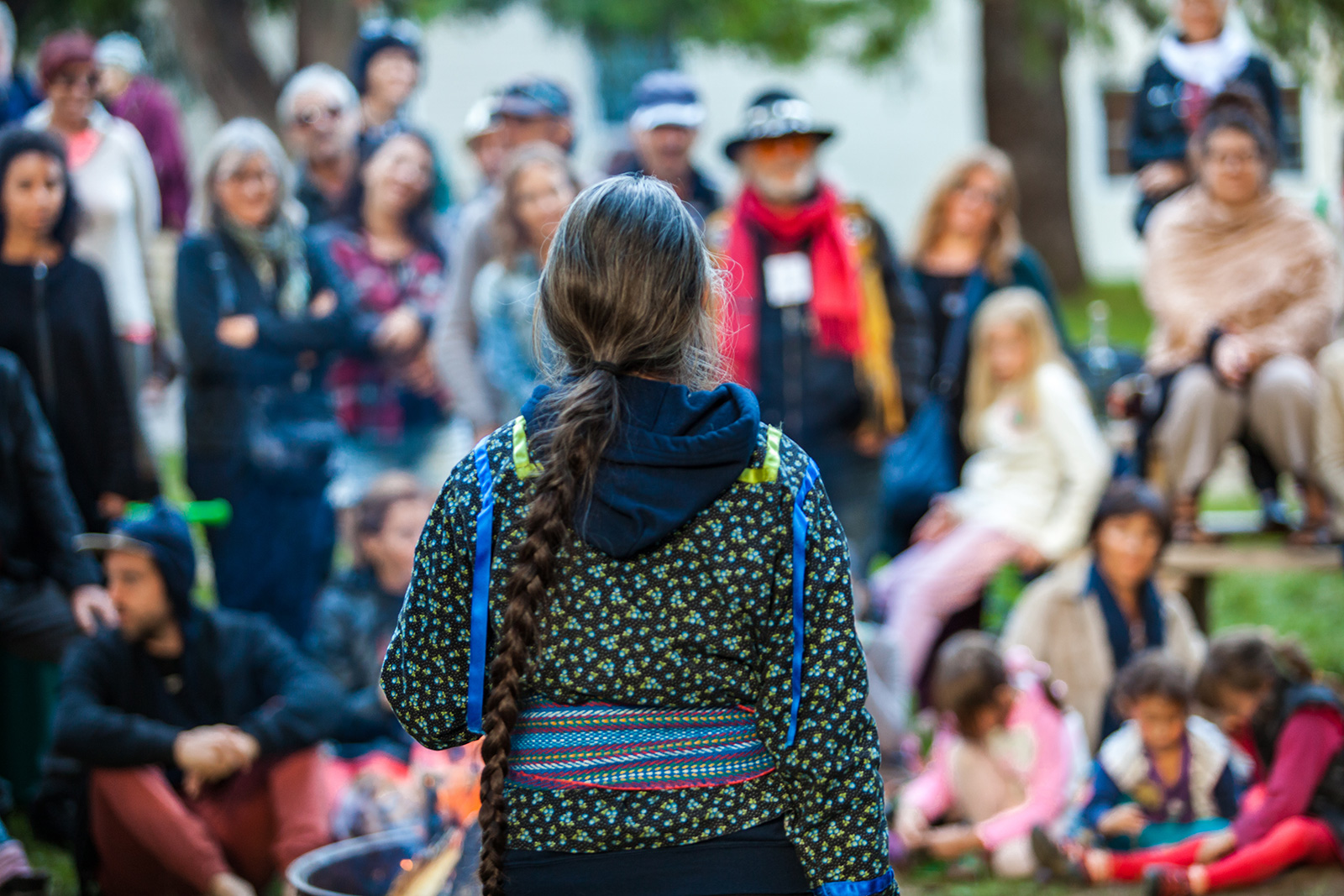 A group of community members gather to discuss the local impact of energy infrastructure projects. Image shows the back of a woman who is speaking to the crowd, with other community members in the middle ground and slightly out of focus. 